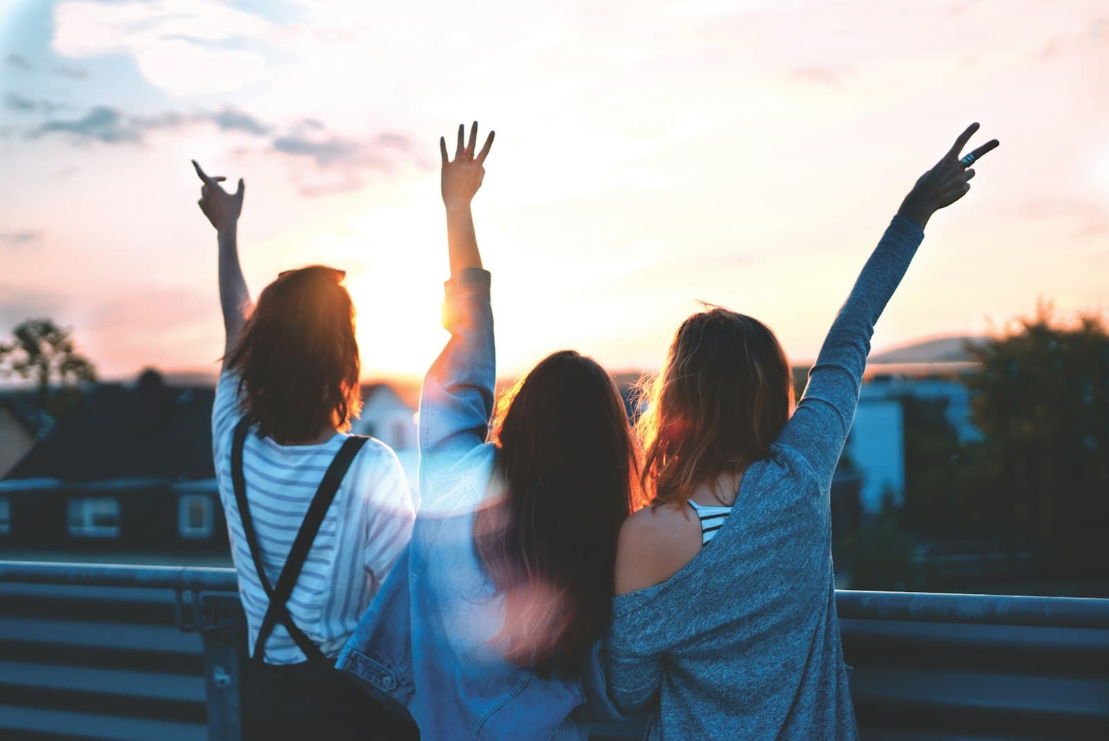Three friends celebrating with arms raised at sunset