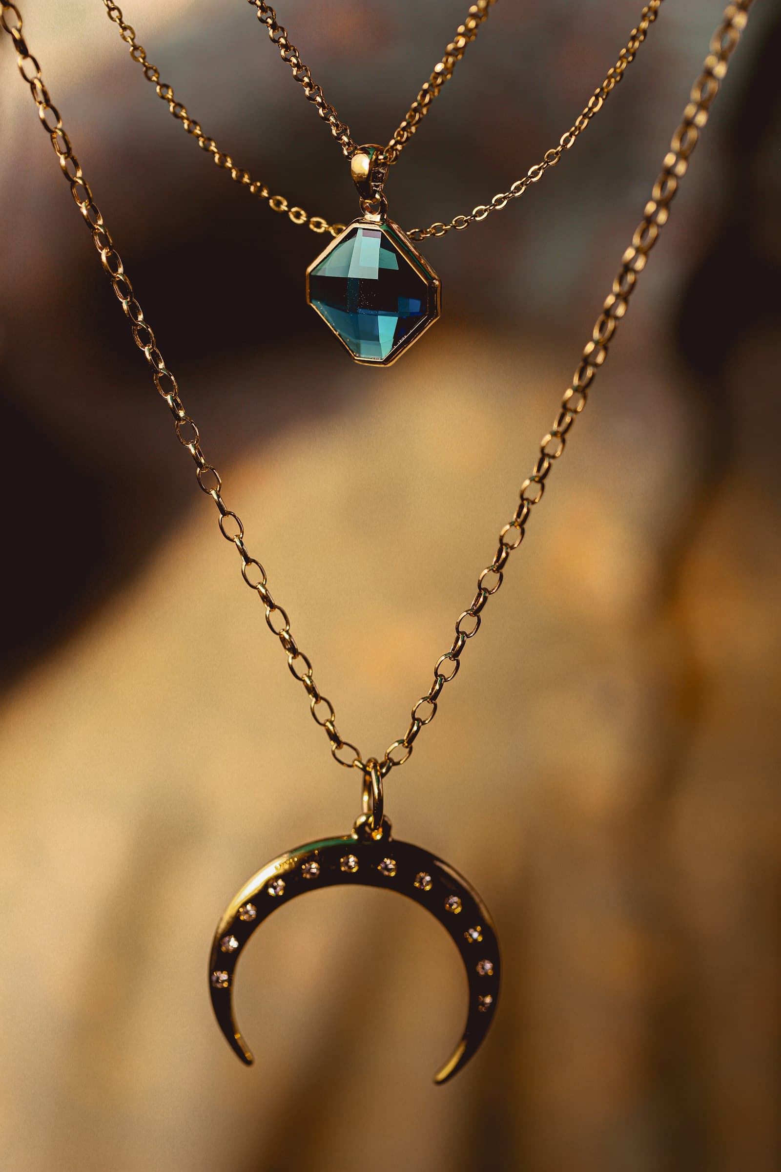 Layered gold necklaces with a blue gem pendant and crescent moon charm