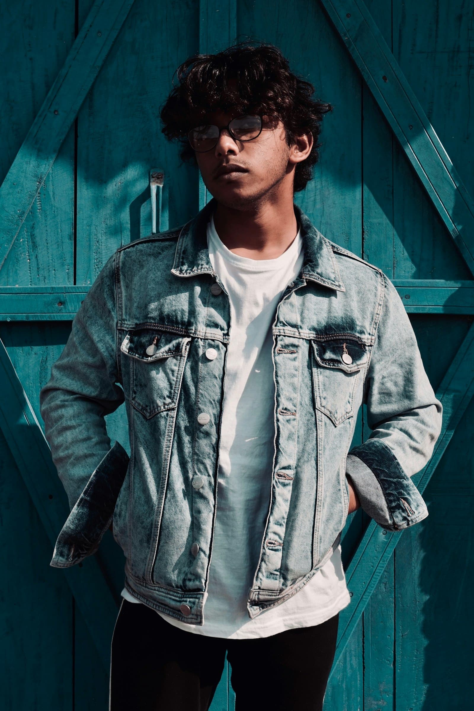 Model in a light-wash unisex denim jacket against a teal door