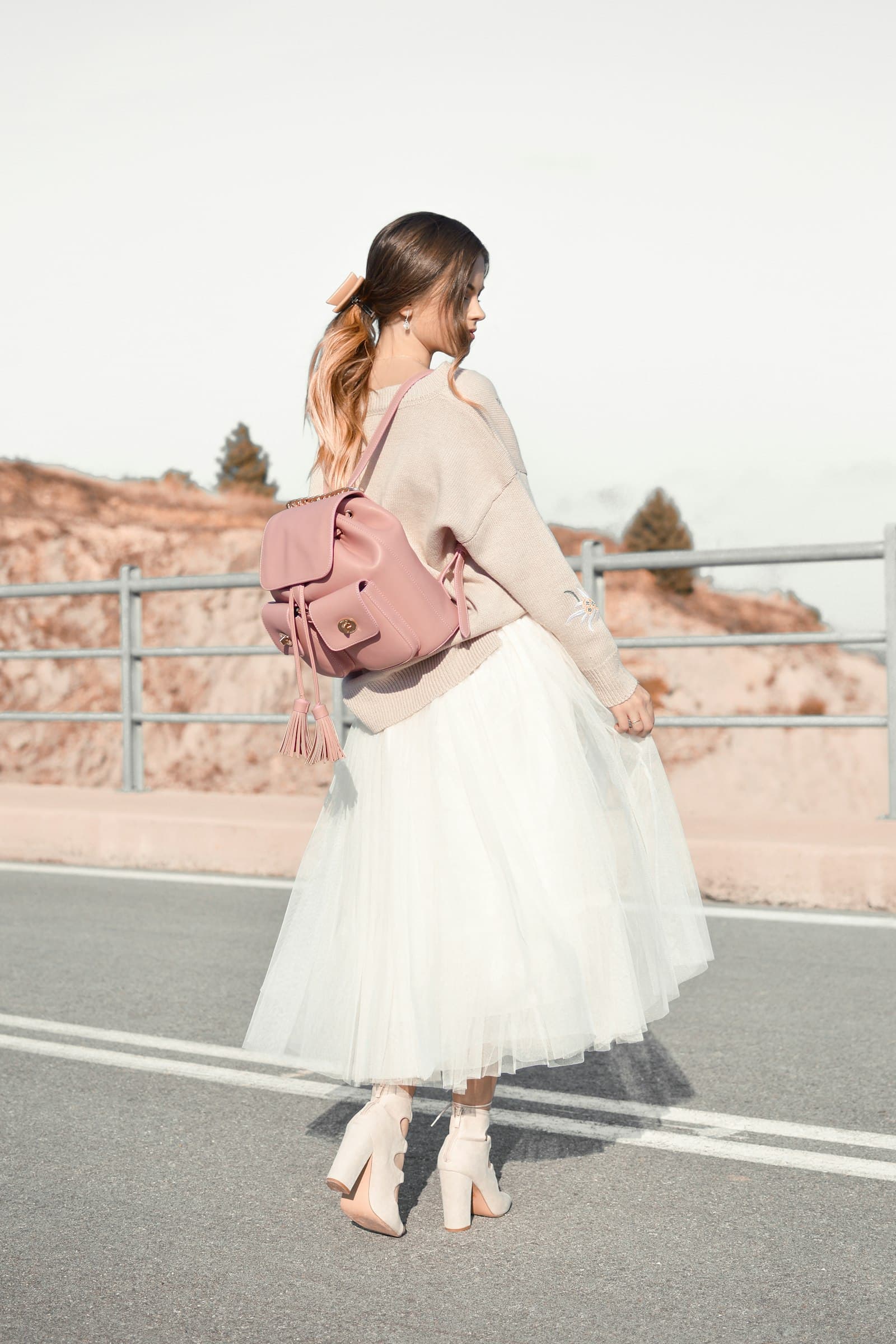 Woman in a white tulle midi skirt and blush sweater with a pink backpack